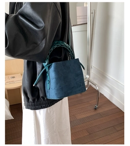 Blue velvet bucket bag with woven handle shown on model in a stylish indoor setting