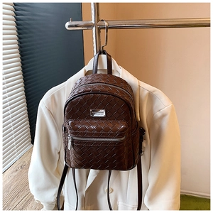 Dettaglio mini zaino marrone scuro intrecciato appeso a un blazer bianco elegante