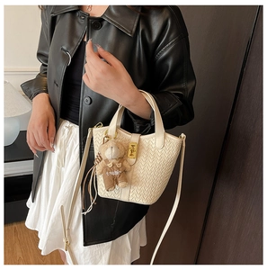 Dettaglio della borsa a secchiello intrecciata beige con chiusura e ciondolo orsetto