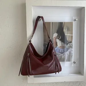 Detail of burgundy hobo bag with parallel zippers and long leather tassels on wall