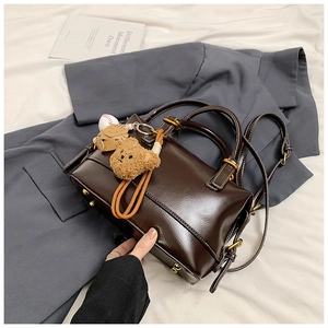 Detail of dark brown Boston bag with teddy bear charm and gold-tone hardware