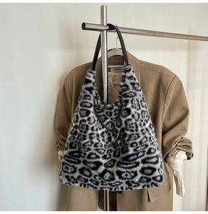 Detail of leopard print plush tote bag with black leather straps hanging on a metal rack