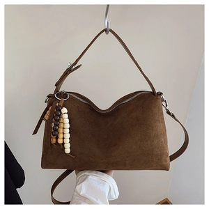 Close-up of dark brown suede shoulder bag with vintage beaded charm and zipper detail