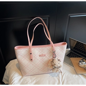 Borsa tote a quadri rosa con tracolla e ciondolo a forma di bambola su una scrivania moderna