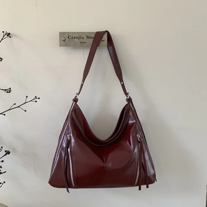 Detail of burgundy patent leather hobo bag with dual vertical zipper tassels