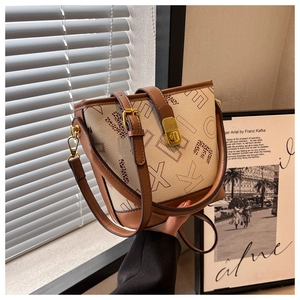 Détail du sac seau montrant la toile beige, les bordures en cuir brun et le fermoir doré