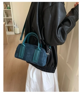 Detail of dark teal suede handbag with leather handles and detachable shoulder strap