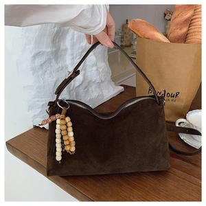 Detailed view of a brown suede bag with wooden bead tassel and silver metal zipper