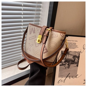 Détail d'un sac seau beige avec bordure en cuir marron foncé et fermoir en métal doré