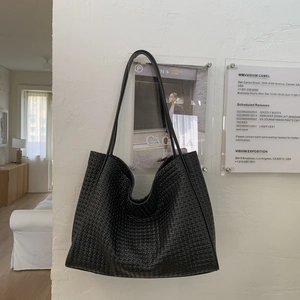 Détail de la texture tressée du cabas en cuir noir et design des fines bandoulières