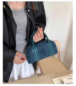 Detail of teal velvet bowling bag with green leather handles held by a model