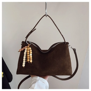 Detail of dark brown suede shoulder bag featuring a wave-shaped top and wooden bead charm