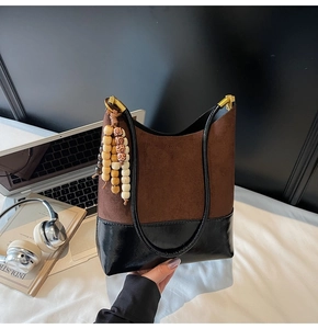 Détail d'un grand sac cabas en daim marron et cuir noir avec un gland en perles