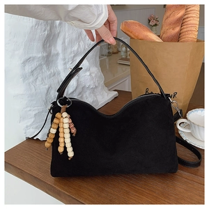 Detailed macro view of black suede retro shoulder bag featuring decorative wooden bead tassel