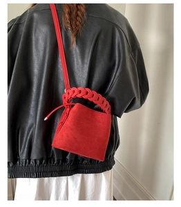 Detail view of the red suede bucket bag with a thick woven handle on a black leather jacket