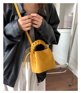 Detail of yellow suede bucket bag featuring a thick braided chain handle and drawstring