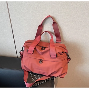 Detail view of brick red nylon travel bag showing zippers and adjustable shoulder strap