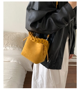 Macro view of mustard yellow suede bucket bag with woven chain handle and drawstring