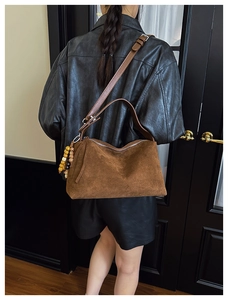 Detail of dark brown faux suede bag with wooden bead charm worn by model in leather jacket