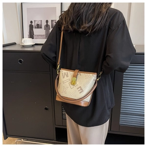 Sac seau chic beige avec bordure marron et motifs de lettres dans un cadre lifestyle