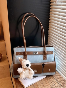 Blue denim tote bag with brown leather handles and cute plush bear charm on desk