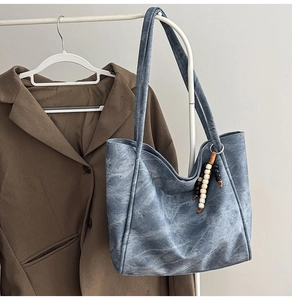 Detail of blue denim tote bag with textured wash finish and elegant beaded tassel charm