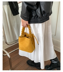 Detail of yellow faux suede bucket bag with a chunky chain handle and drawstring closure