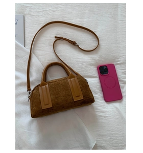 Detail view of brown suede bowling bag featuring leather handles and silver hardware