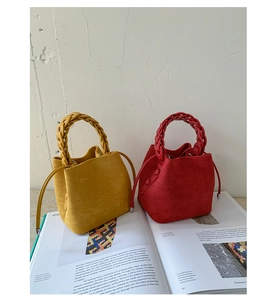 Close-up of suede bucket bags featuring woven handles and drawstring in red and yellow