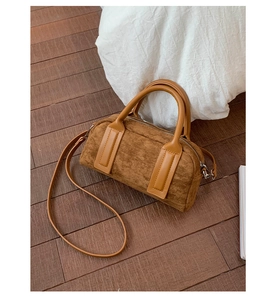 Close-up of a brown suede Boston bowling bag with dual handles and a long strap