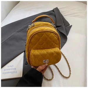 Macro detail of mustard yellow quilted mini backpack with chain strap on white bedding