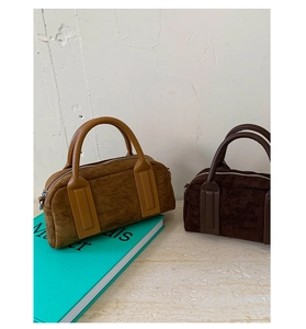 Close-up of vintage suede bowling bags in tan and dark coffee on marble surface
