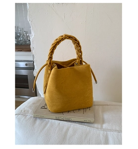 Close-up of yellow suede bucket bag featuring a thick woven handle and drawstring detail