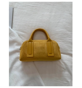 Detailed top view of a yellow suede bowling bag with leather handles on white fabric