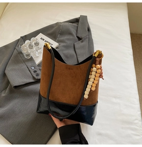 Détail du sac seau bicolore en daim marron et cuir noir, avec pendentif en perles de bois