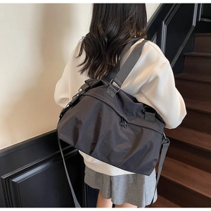 Rear view of a model wearing a large black nylon tote bag with a grey wide strap