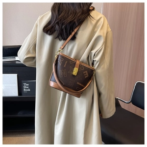 Détail du sac seau marron rétro avec imprimé monogramme et fermoir doré sur un mannequin