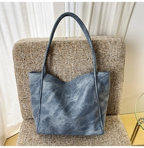 Blue-grey tote bag with marble wash texture placed on a stylish woven chair