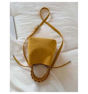 Detail of ginger suede bucket bag featuring a handcrafted woven handle and side ties