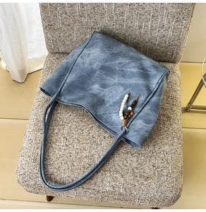 Close-up of washed denim blue tote bag with unique beaded charm on a textured chair