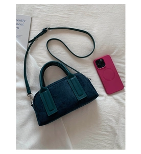 Flat lay of navy blue suede handbag with green leather handles and adjustable strap