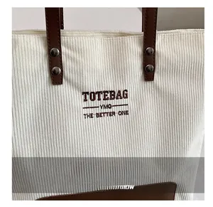 Dettaglio borsa tote in velluto bianco con manici in pelle marrone e testo ricamato