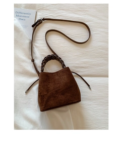 Close-up of a dark brown suede bucket bag with woven ring handle and adjustable strap