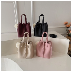 Detail of four bucket bags in lychee leather featuring plush pompom charms and straps