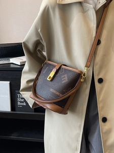 Sac seau vintage à monogramme avec finitions en cuir et boucle dorée porté sur un manteau