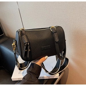 Détail d'un sac cylindre en cuir noir avec large bandoulière contrastée et finitions dorées