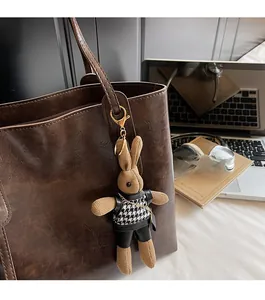 Dettaglio di un ciondolo a coniglio in peluche con gilet pied de poule su borsa in pelle
