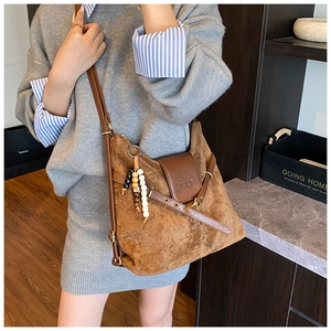 Détail d'un sac dumpling en daim marron avec rabat en cuir et accessoire de charme perlé