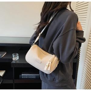 Détail du sac baguette blanc crème avec texture cuir grainé et breloques à pompons
