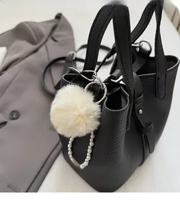 Detail of plush pompom charm and pearl chain on a black pebbled leather bucket bag